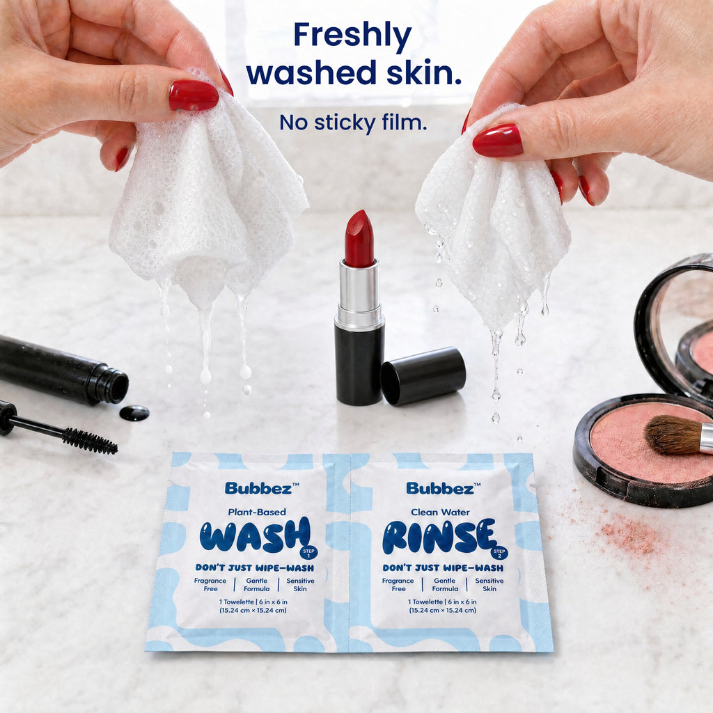 Two hands hold a lathering Bubbez WASH wipe and a dripping RINSE wipe above a marble vanity set with lipstick, mascara and blush. A WASH and RINSE twin sachet lies below. Headline reads Freshly washed skin. Not wiped.