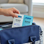 Hand holding Bubbez soap and rinse packets over a blue bag.