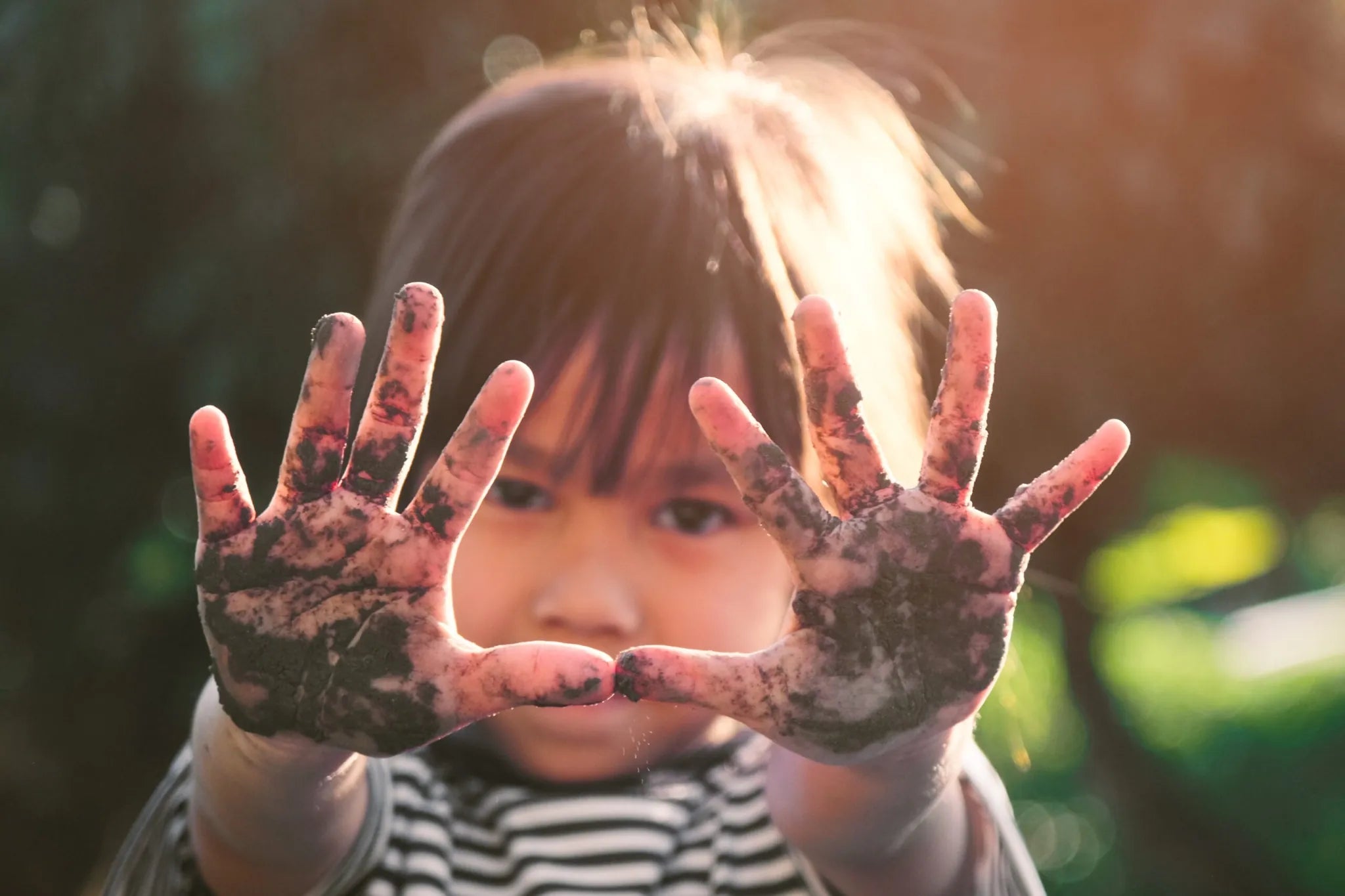 Child with dirty hands in front of a blurred natural background