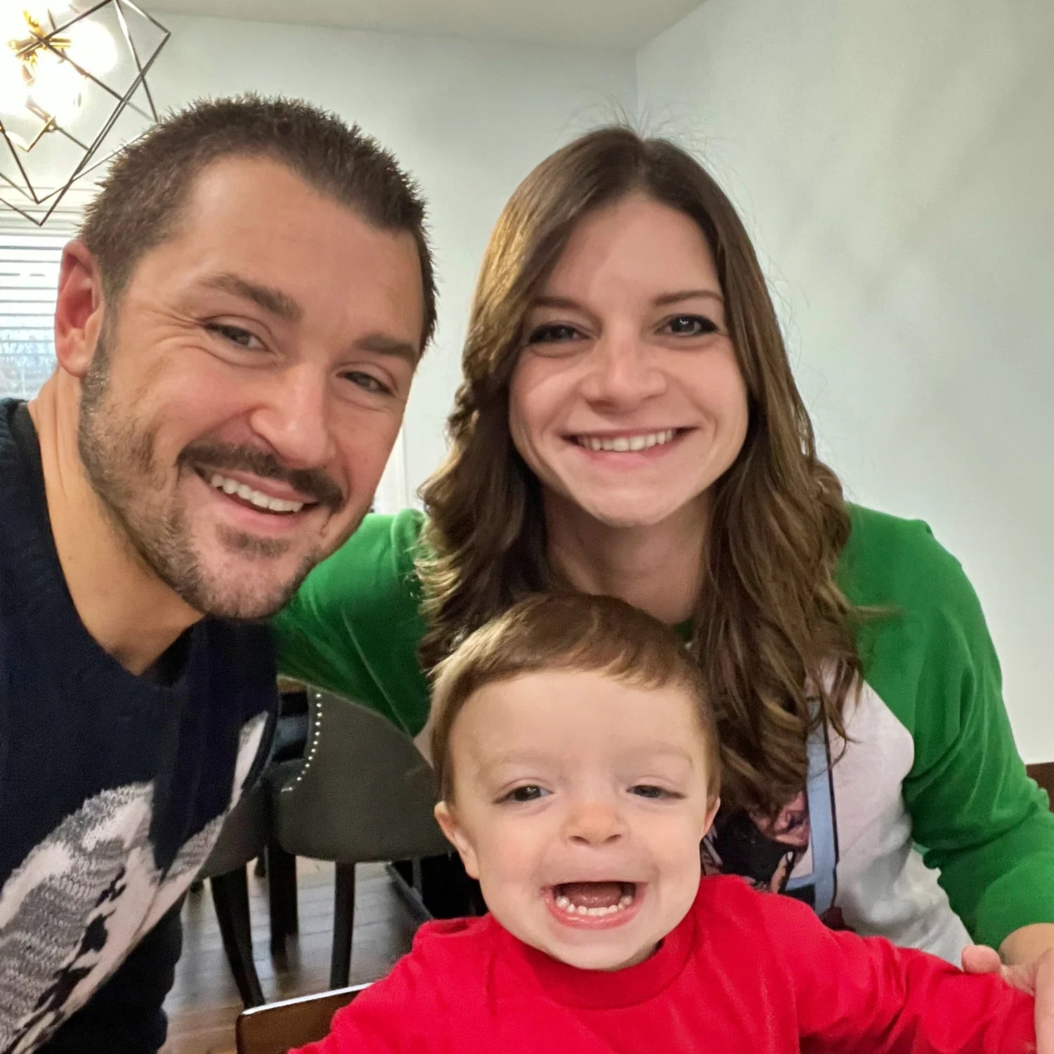 Family of three smiling indoors, likely in a home setting.