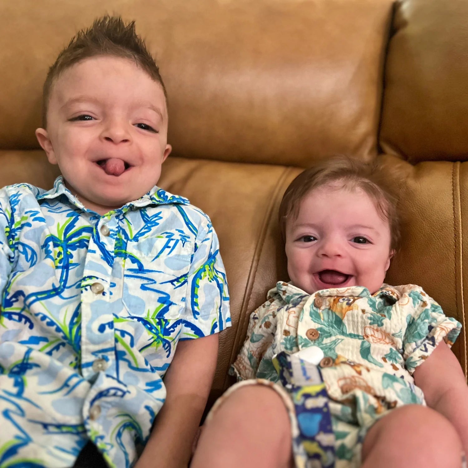 Two children sitting on a brown couch, one wearing a colorful shirt and the other in a patterned outfit.