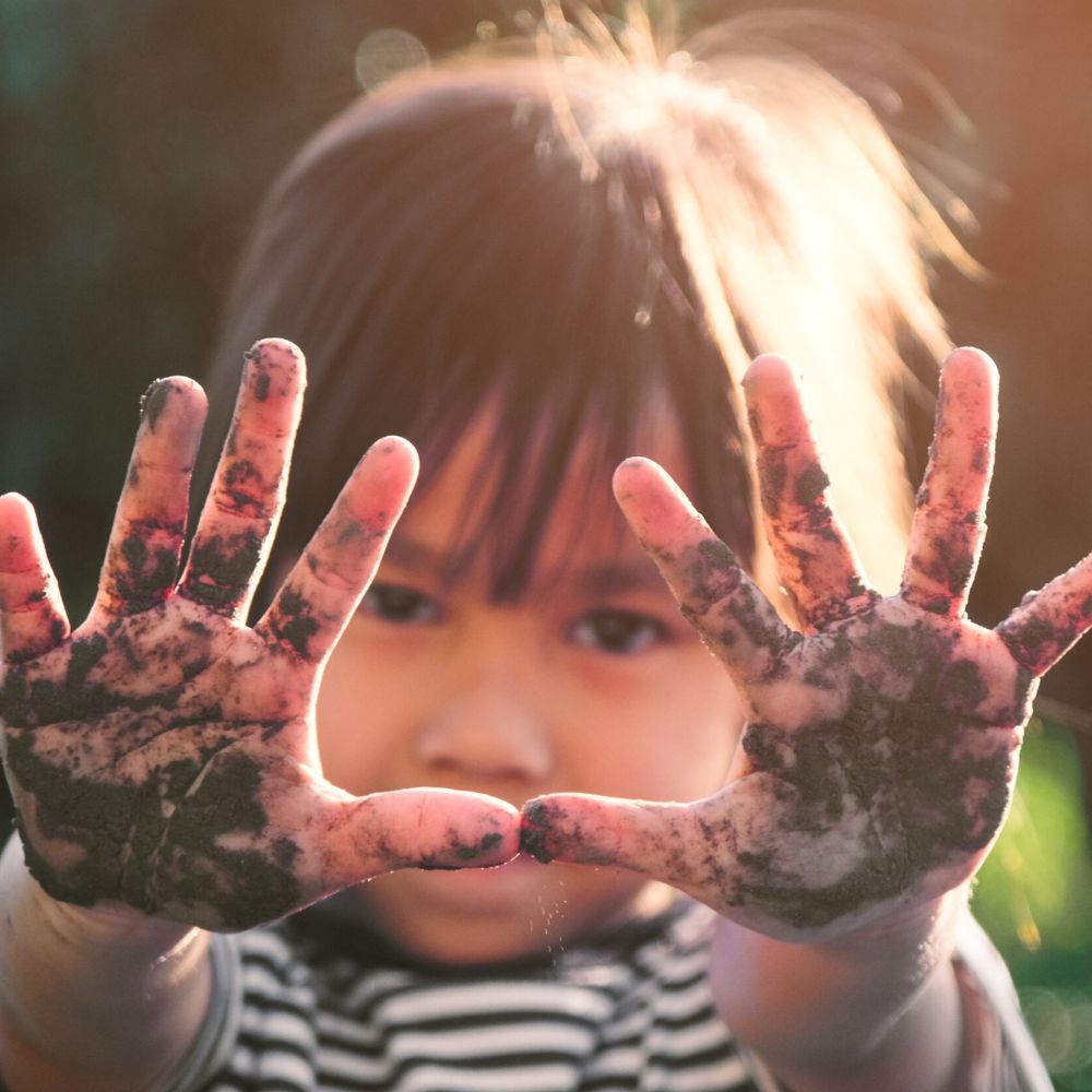 Child with dirty hands up to the camera, sunlit background