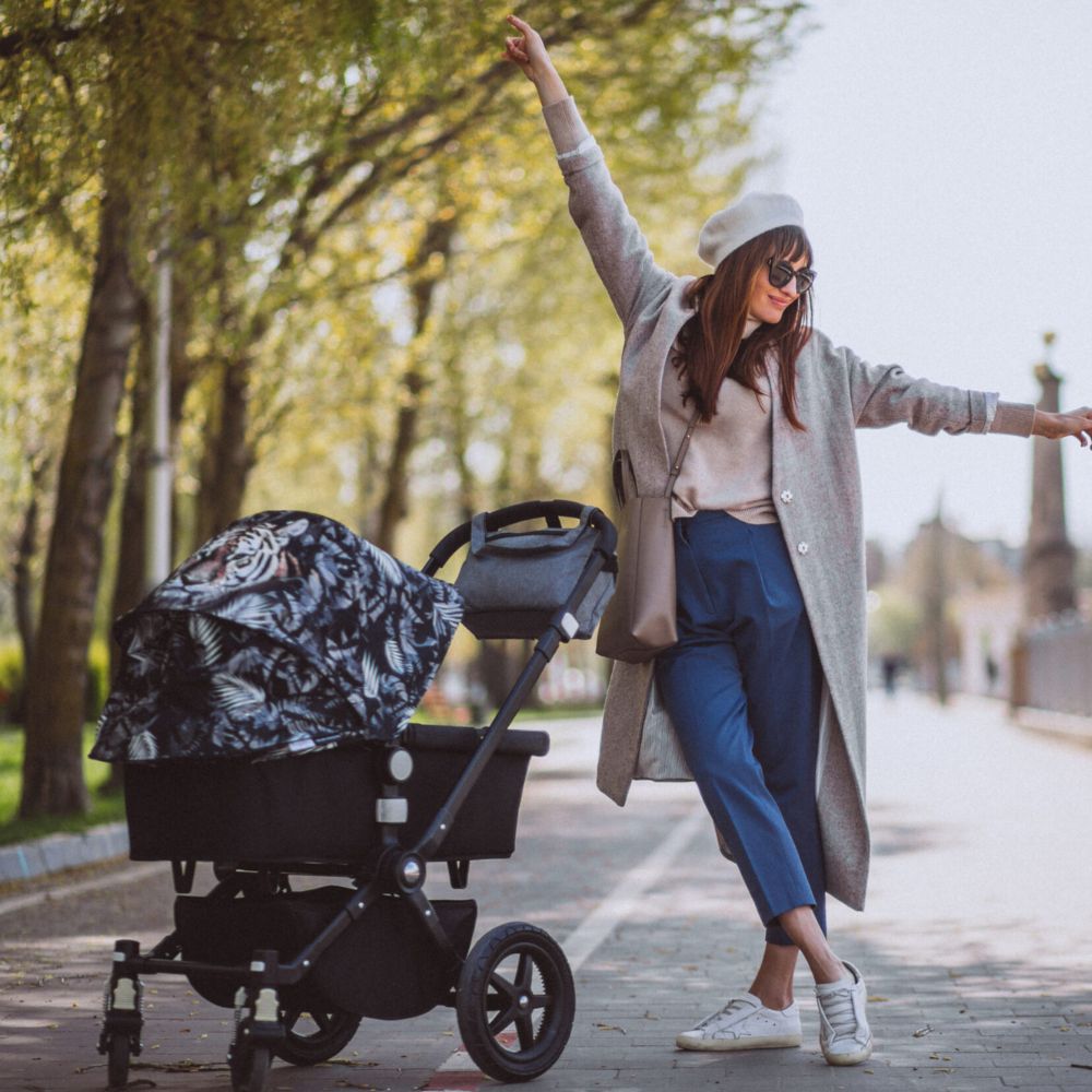 Woman in a long coat and sunglasses standing next to a stroller on a transparent background