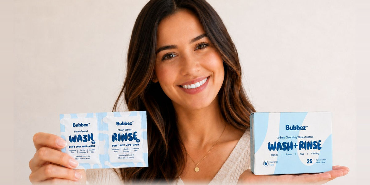 A woman holds a Bubbez WASH and RINSE twin sachet in one hand and the 25 count retail box in the other, against a plain neutral wall.